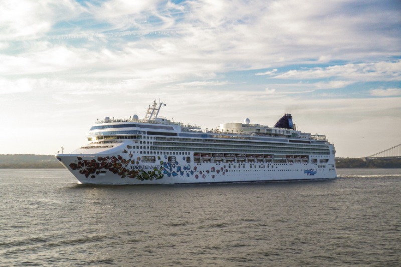 A large cruise ship gracefully sails on a calm sea under a bright sky.