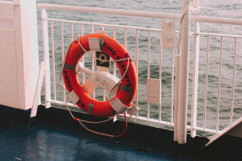 Red lifebuoy hanging on a ship's railing with a calm ocean backdrop.