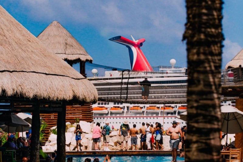 Crowd enjoying a sunny day at tropical resort near a cruise ship.