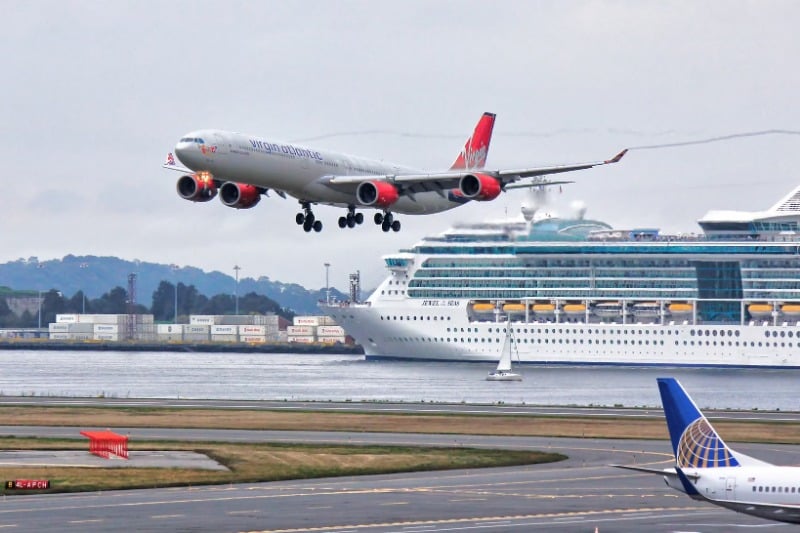 A thrilling view of an airplane landing with a cruise ship passing by in Boston Harbor.