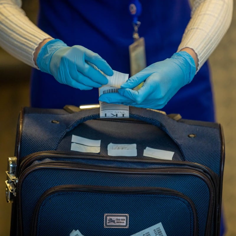 Close-up of airport security process with gloved hands inspecting luggage tags.