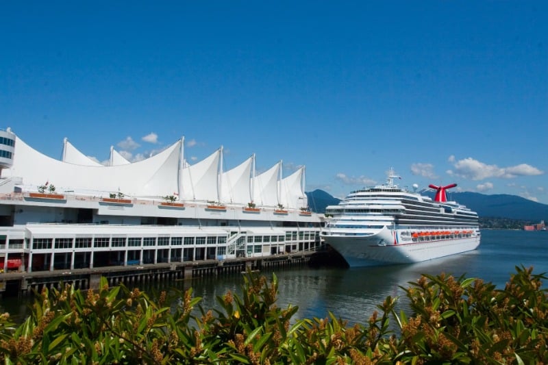 A cruise ship is docked at Canada Place in Vancouver on a sunny day, showcasing the iconic sails.