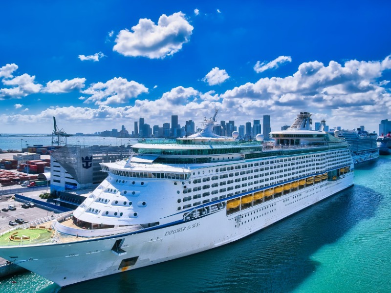 A luxurious cruise ship moored at the bustling Miami port with the city skyline in the background.