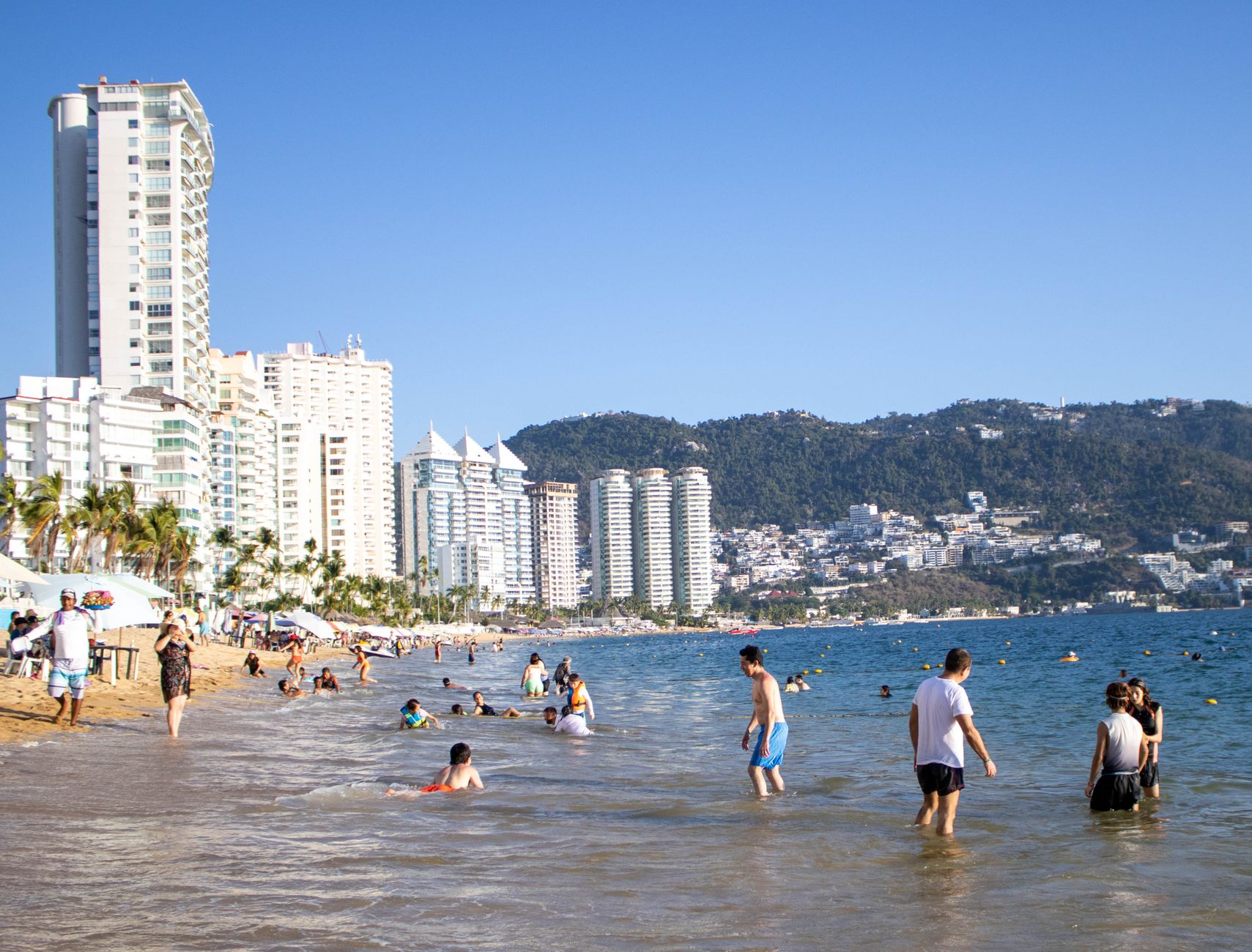 Vibrant beach scene at Acapulco, Mexico with people enjoying the sunny coastline.