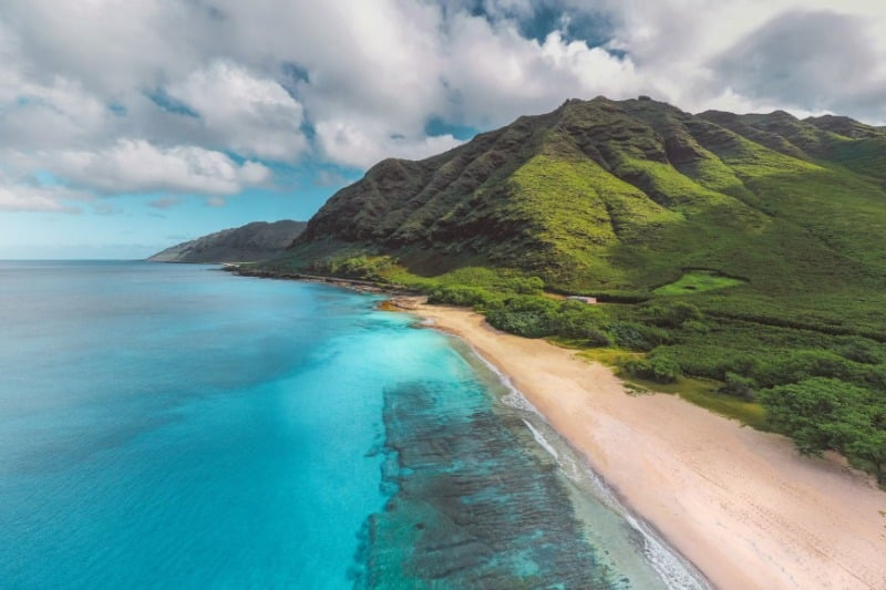 Stunning aerial view of a vibrant Hawaiian coastline with lush mountains and crystal-clear waters.